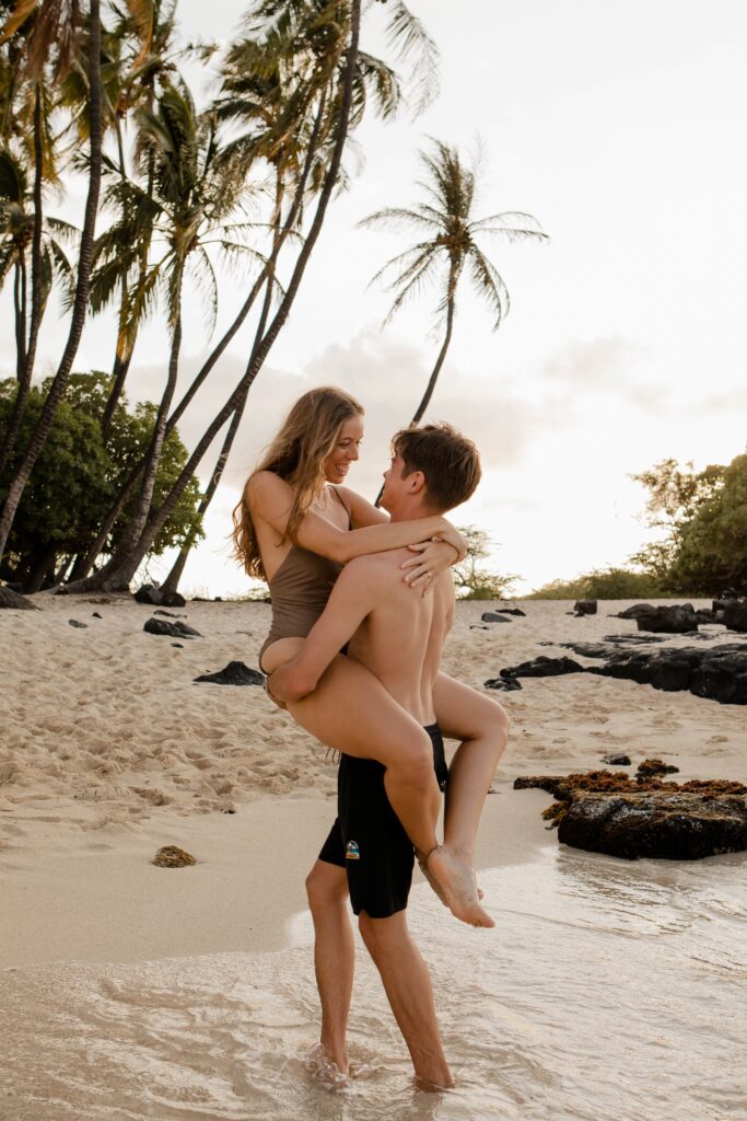 husband picking up wife on beach with palm trees in background engagement photographer hawaii