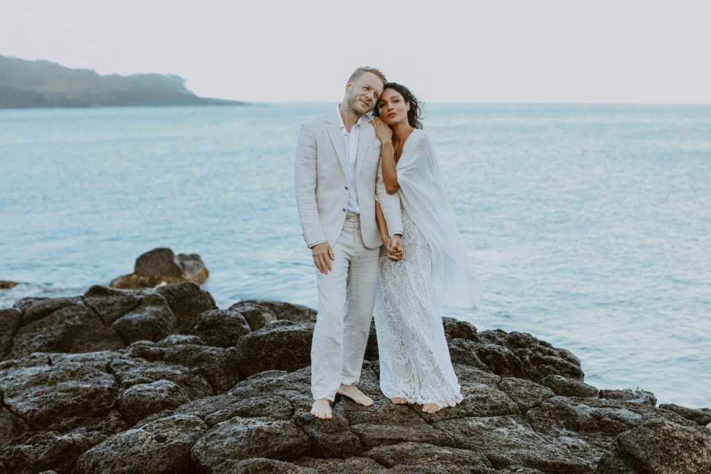 couple hugging on lava rock in front of ocean Hawaii elopement photographer