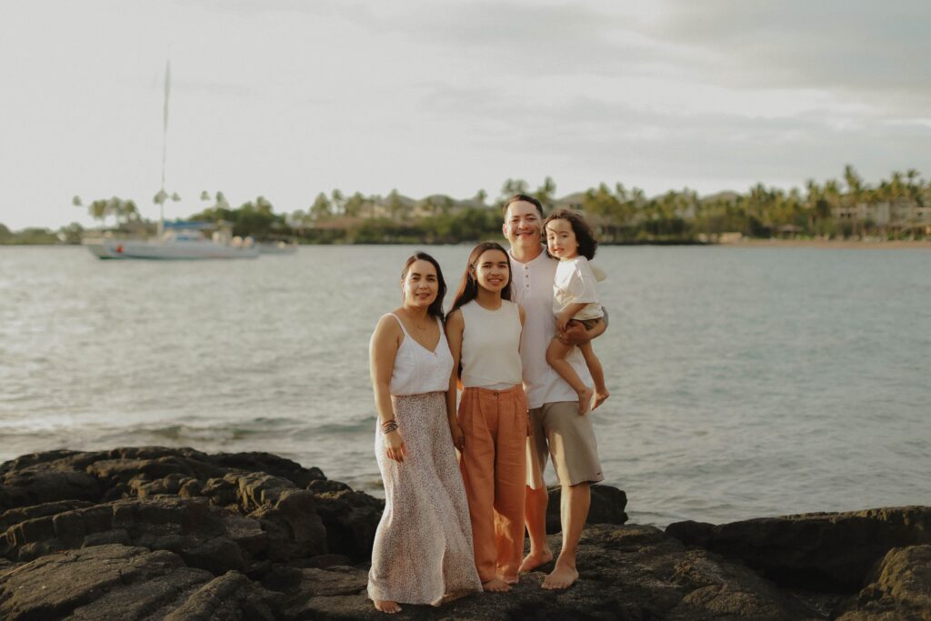 Family standing on lava rocks in front of ocean in Hawaii